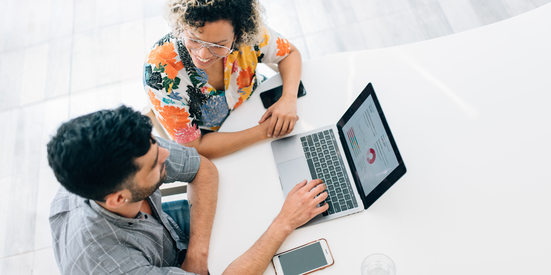 Two business professionals collaborating at a table while reviewing analytics charts on a laptop.
