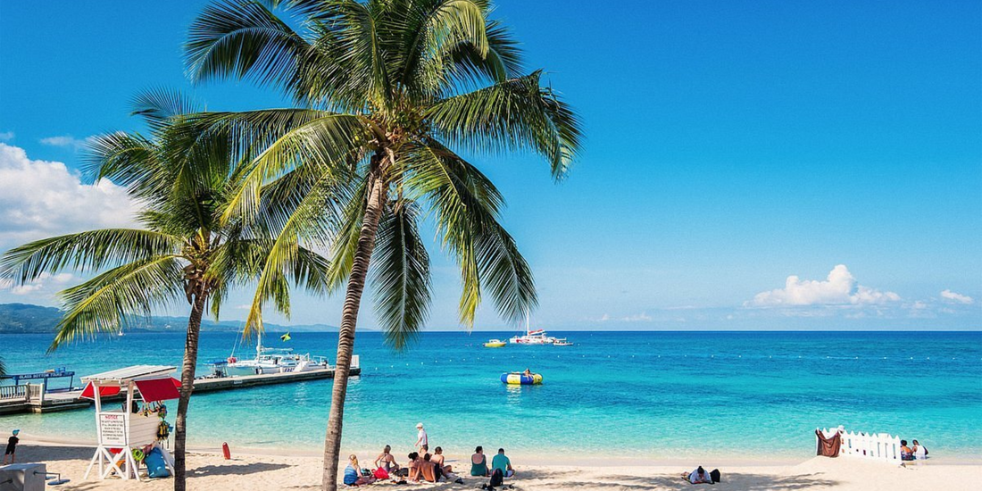 Tropical beach in Jamaica with palm trees, white sand, turquoise water, and visitors relaxing by the sea.