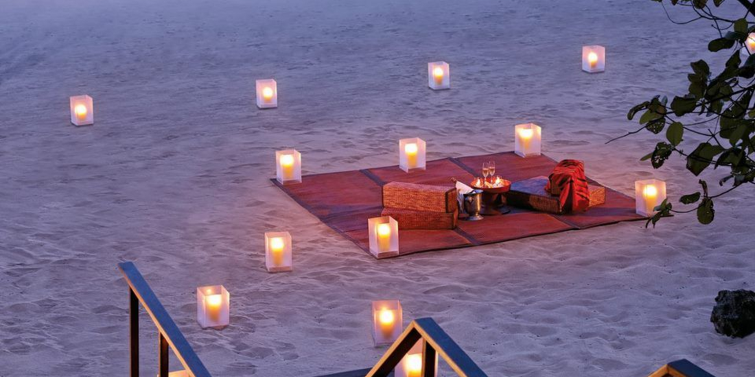 Romantic beachfront setup illuminated by numerous square paper lanterns on the sand at twilight.