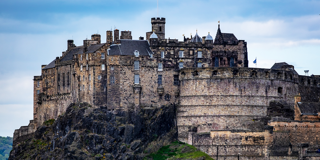 Edinburgh Castle, a historic fortress, perched dramatically atop an ancient volcanic crag under a muted blue sky.