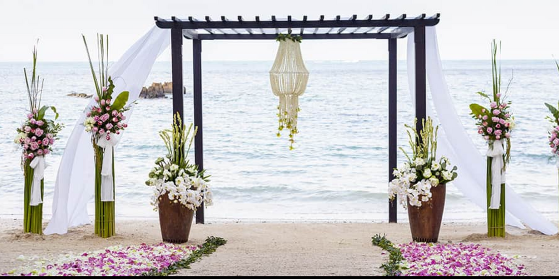 Elegant wedding archway on the beach, adorned with lush floral displays and a delicate beaded chandelier.