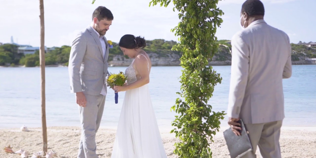 A couple exchanges vows on a tropical beach, framed by lush greenery.