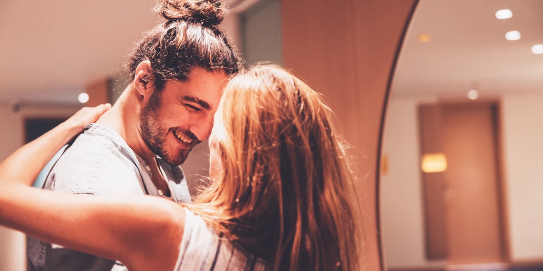 Close-up portrait of a smiling man embracing a woman with long red hair indoors.