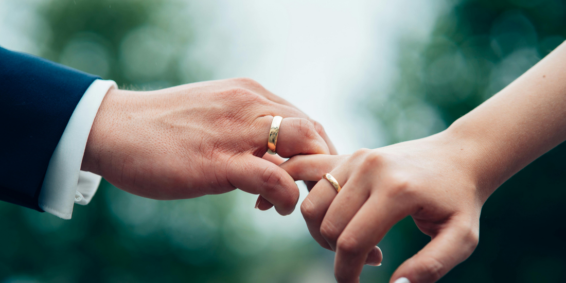 Close-up of two hands, fingers intertwined, showcasing wedding rings.