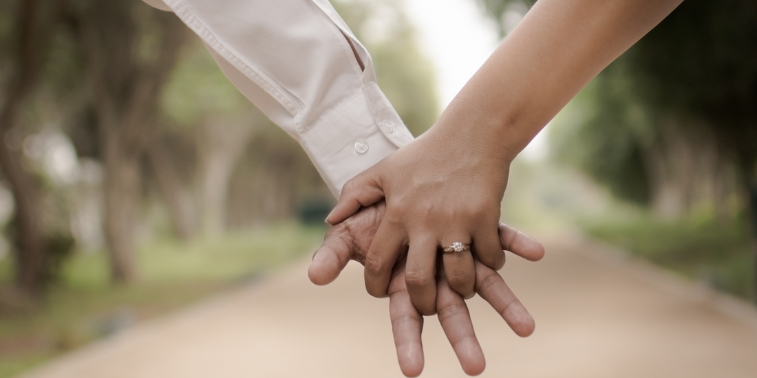 A symbol of commitment: a hand adorned with an engagement ring clasped with another.
