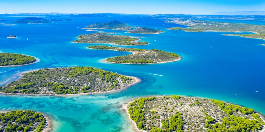 Aerial view of a bright blue sea dotted with densely vegetated islands under a clear sky.
