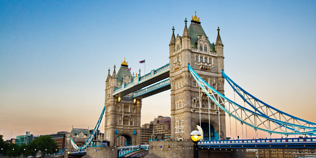 The iconic Tower Bridge in London featuring its Victorian Gothic architecture under a clear, pale blue sky at dusk.