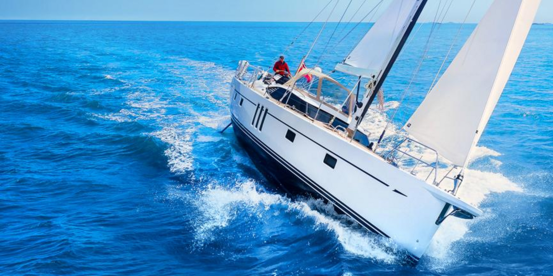 A modern white sloop sailboat cutting sharply through deep blue, choppy ocean water under full sail.