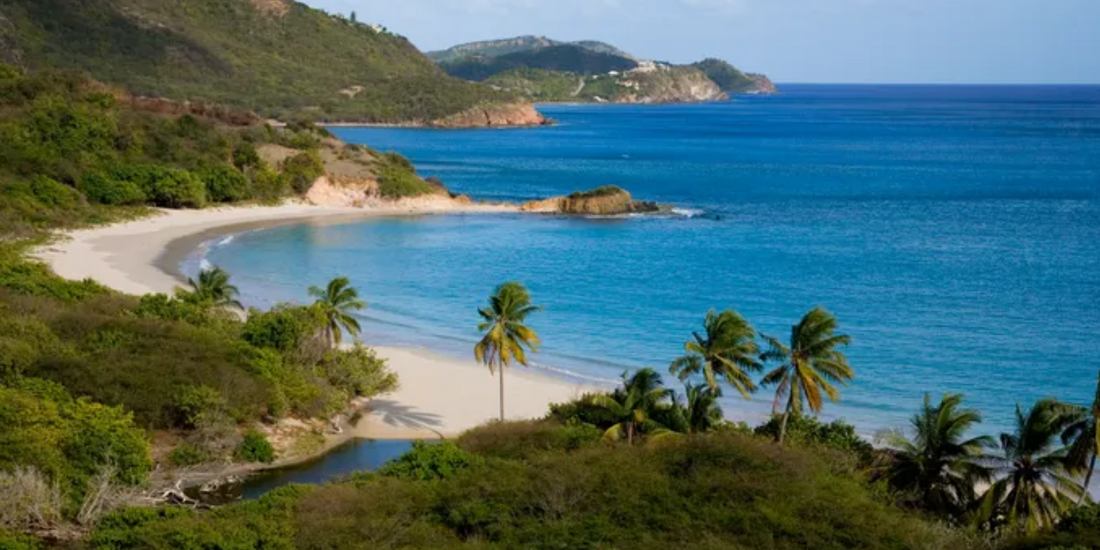 Aerial view capturing a secluded, crescent-shaped beach bordered by lush green hills and vivid turquoise ocean water.