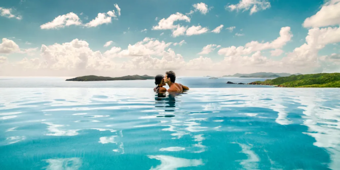 Couple relaxing in an infinity pool overlooking the British Virgin Islands, surrounded by turquoise water, distant islands, and a bright Caribbean sky.