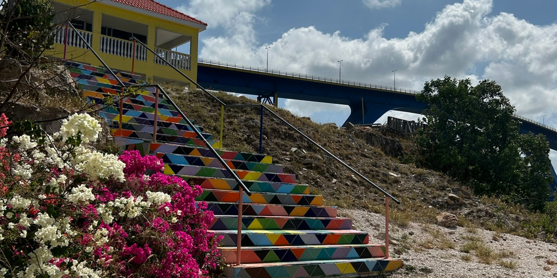 Colorful tiled staircase in Curacao with yellow building and blue bridge.