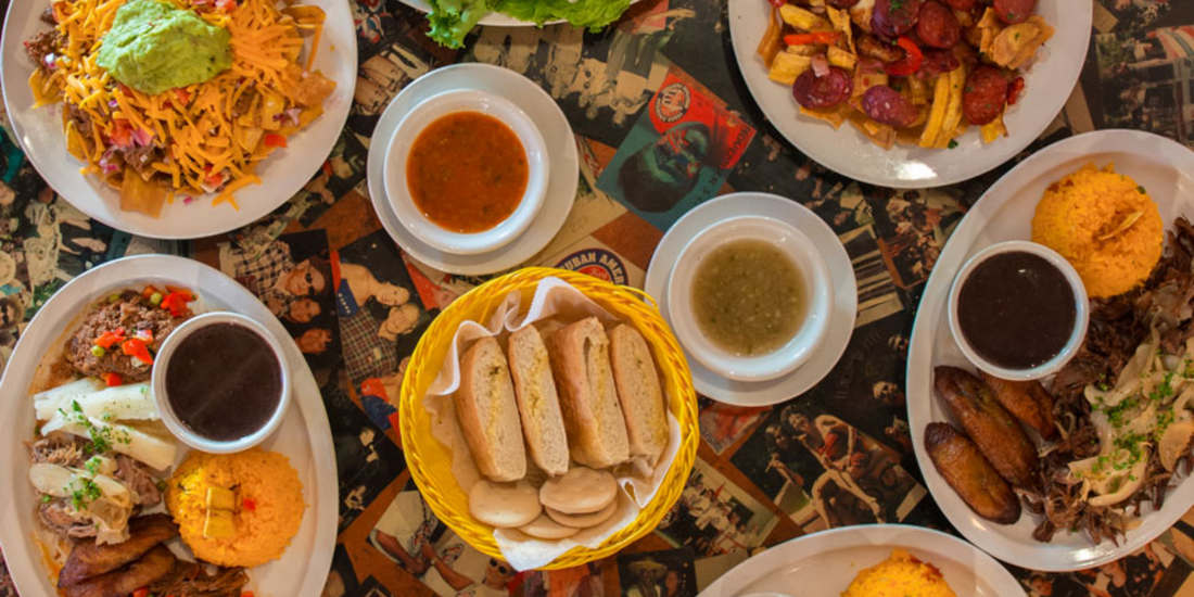 Traditional Cuban dishes including rice, beans, plantains, roasted meats, and bread served on a rustic table