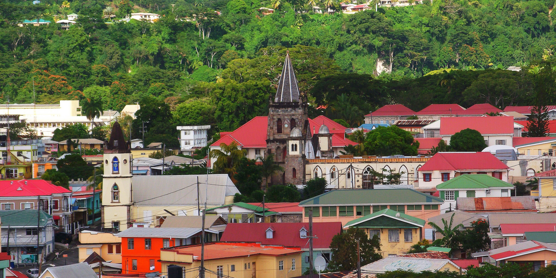 Colorful rooftops and historic architecture in Roseau, Dominica surrounded by lush rainforest hills.