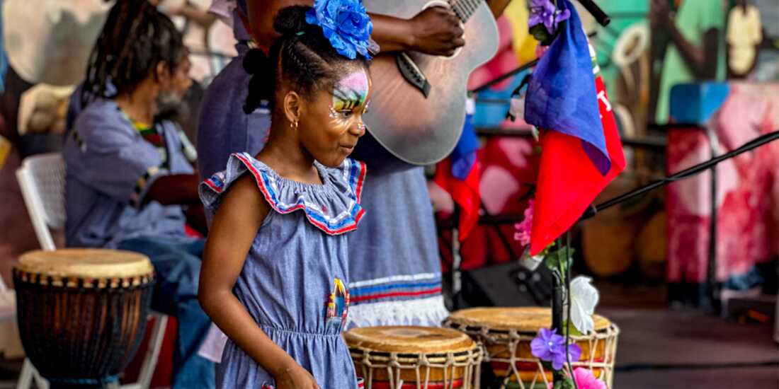 Young girl with face paint playing drums during a Haitian cultural music performance with live musicians