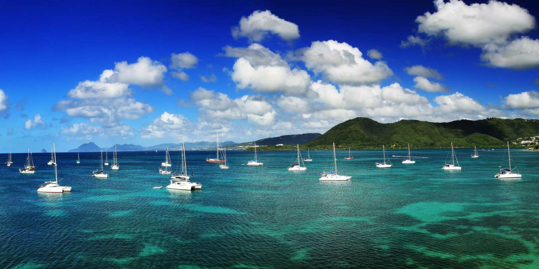 Sailboats anchored in clear turquoise water along the coast of Martinique with green hills in the background